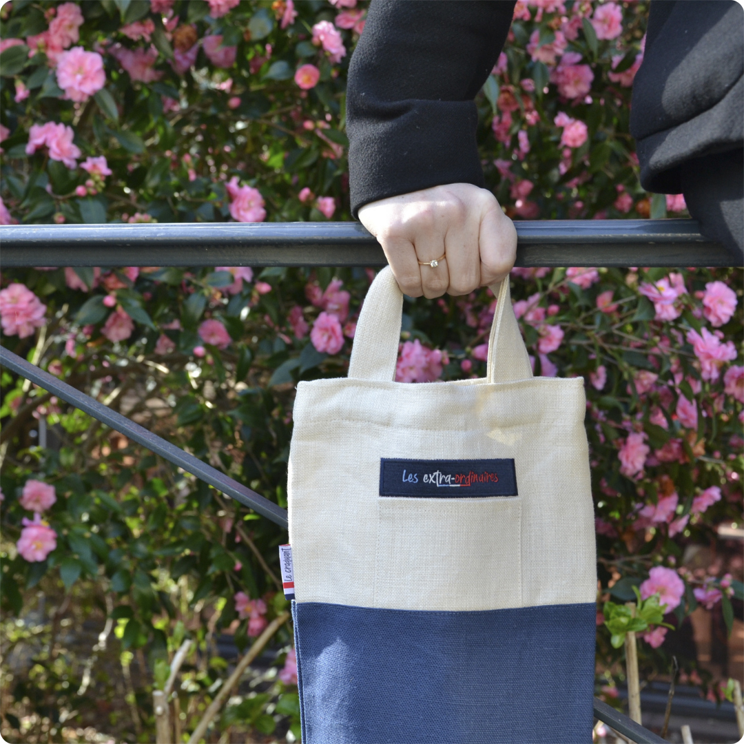 Sac à pain le craquant bleu tenu par une femme devant un buisson en fleurs