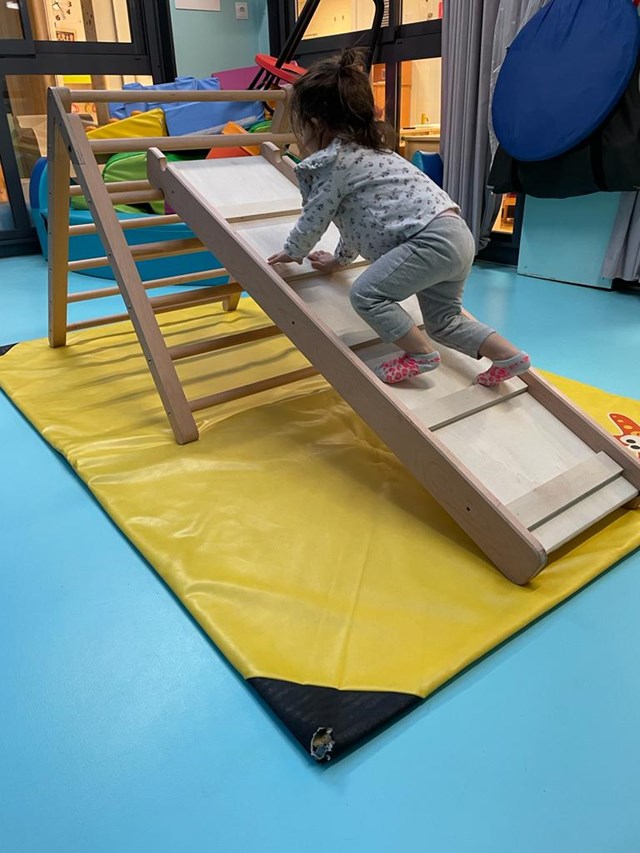 Enfant grimpant sur le toboggan du triangle de motricité libre en bois