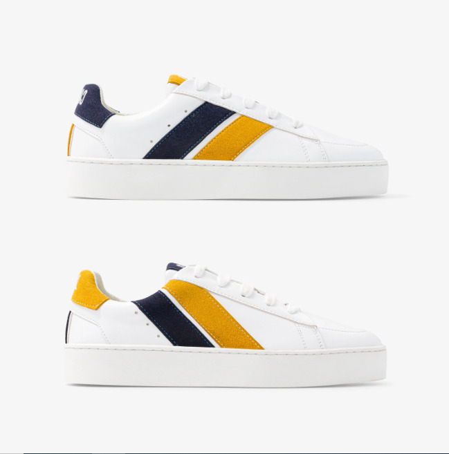 baskets en cuir blanches avec deux rayures asymétriques noir et jaune. Logo à l'arrière.