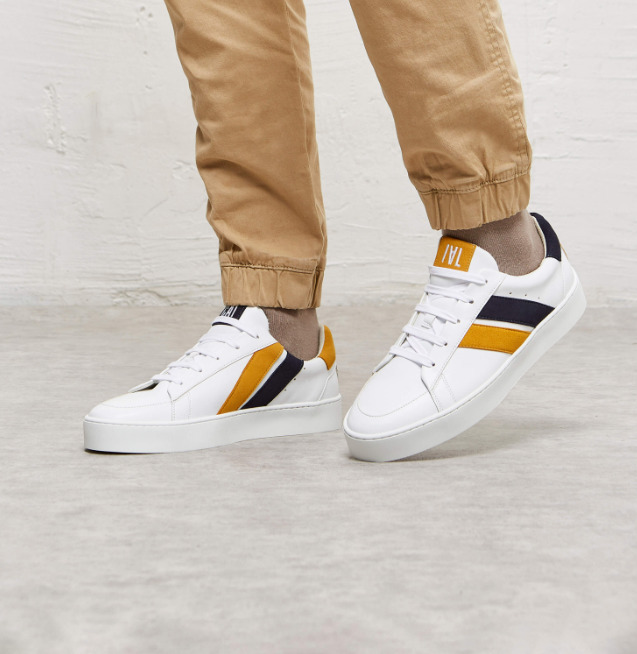 baskets en cuir blanches avec deux rayures asymétriques noir et jaune. Logo à l'arrière.
