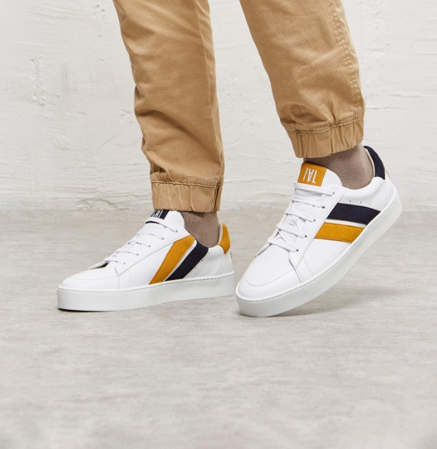 baskets en cuir blanches avec deux rayures asymétriques noir et jaune. Logo à l'arrière.