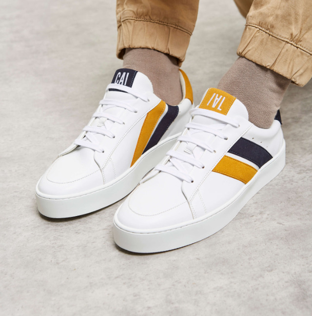 baskets en cuir blanches avec deux rayures asymétriques noir et jaune. Logo à l'arrière.